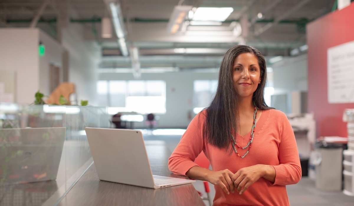 blog cover woman in orange top standing in office with a laptop